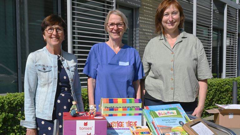 Andrea Niedermaier (li.) und Petra Höckl (re.) übergaben die Audio-Boxen und dazu passende Figuren, Bücher, Puzzles sowie Malstifte und -blöcke an Stationsleiterin Regina Borsutzky.